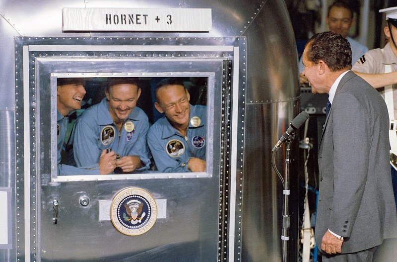 24 lipca 1969 roku, prezydent USA, Richard Nixon, rozmawia z członkami misji Apollo 11, zamkniętymi w hermetycznie szczelnej kapsule bezpieczeństwa, na pokładzie okrętu USS Hornet